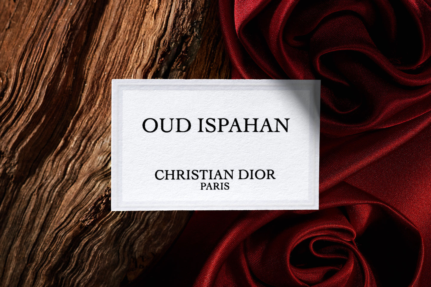 "Elegant Oud Ispahan Dior Perfume label on textured wood background with rich red silk fabric, showcasing Christian Dior Paris luxury branding"
