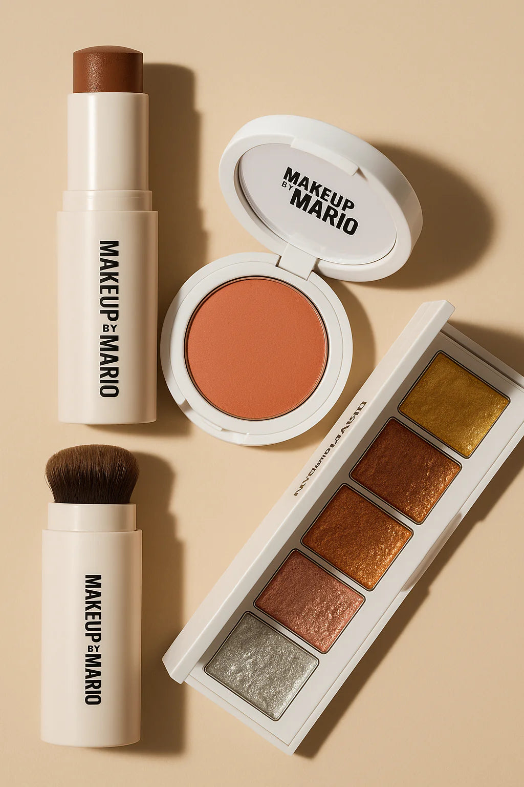 Makeup by Mario products including contour stick, blush compact, and metallic eyeshadow palette displayed on a beige background with soft lighting.