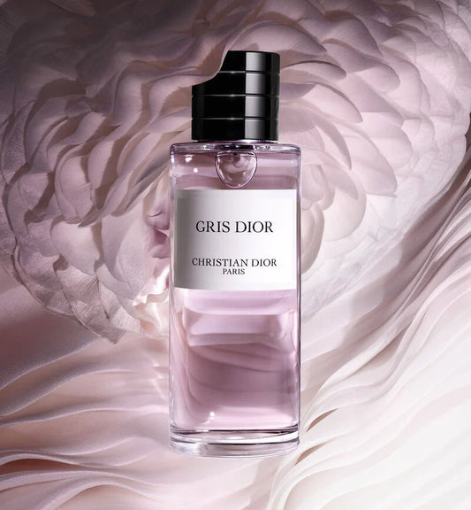 Crystal bottle of Gris Dior perfume with soft pink liquid against delicate rose petal backdrop, highlighting this exclusive Dior perfume's elegance.