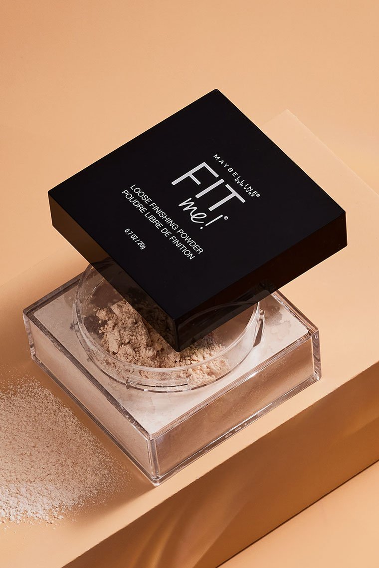 Artistic product shot of the Maybelline Fit Me Loose Face Powder with its open container and lid on a beige background