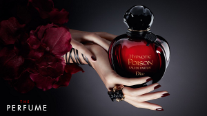 Elegant hand holding Dior Hypnotic Poison perfume 100ml bottle against dark background with red floral elements.